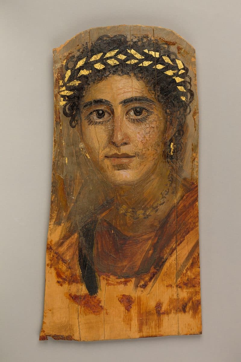 Painted wooden panel portrait of a young woman with dark curly hair, a gilded wreath, gold earrings and a red garment, looking straight out